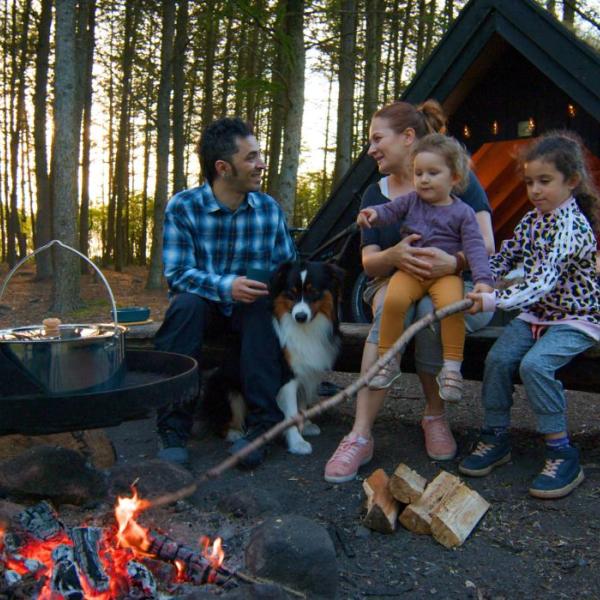 Eltern und Kinder genießen das Feuer an einem Schutzplatz und kochen über dem Feuer