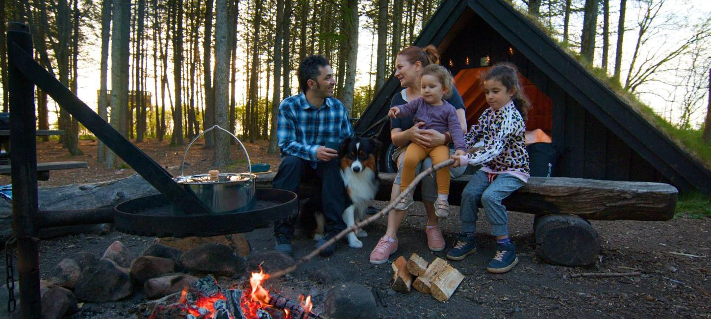 Eltern und Kinder genießen das Feuer an einem Schutzplatz und kochen über dem Feuer