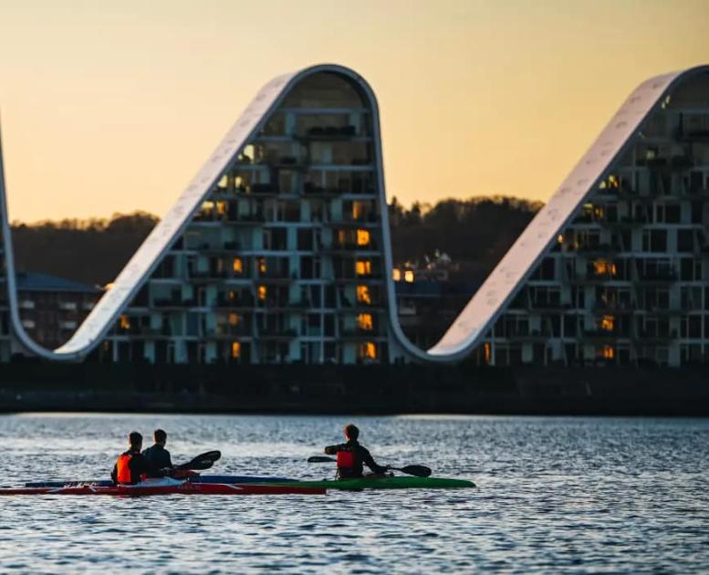 Menschen in Kajaks auf dem Vejle-Fjord mit Bølgen (der Welle) im Hintergrund